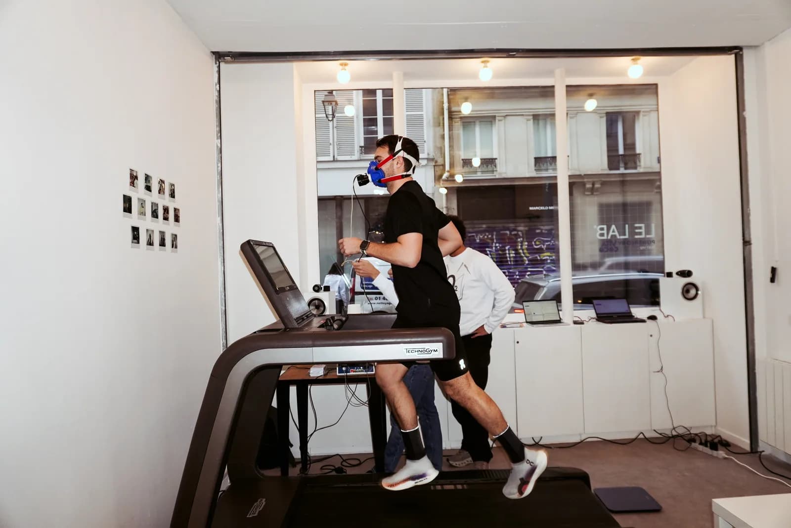 Un athlète court sur le tapis du LAB, masque d'analyse des gaz au visage, le testeur à côté de lui